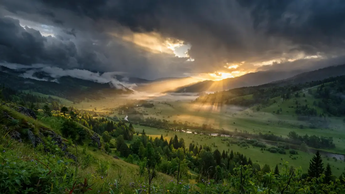 Sunrise breaking through dark storm clouds over a quiet valley