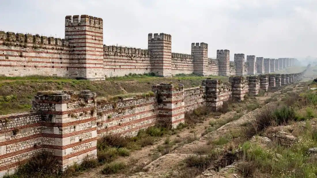 The triple-line Theodosian land walls of Istanbul, stone towers and red-brick bands stretching into the distance under a pale sky