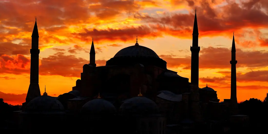 Hagia Sophia's great dome and minarets silhouetted against a dramatic orange sunset sky