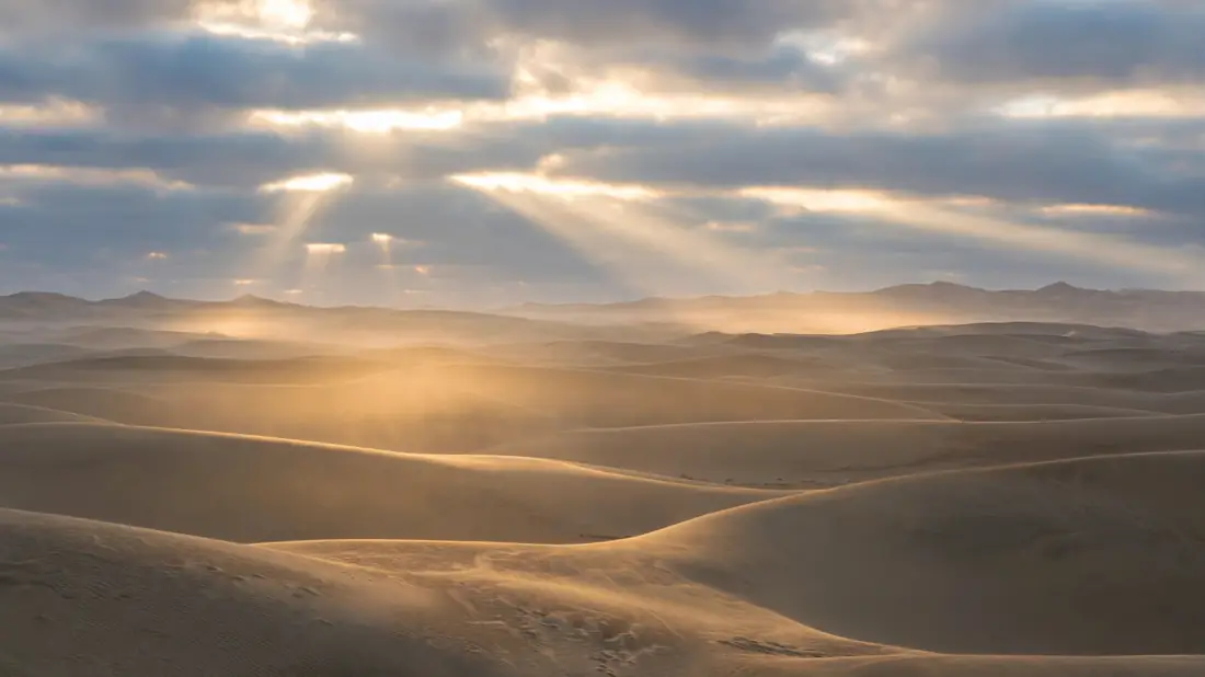 Soft morning light breaking through clouds over a quiet desert