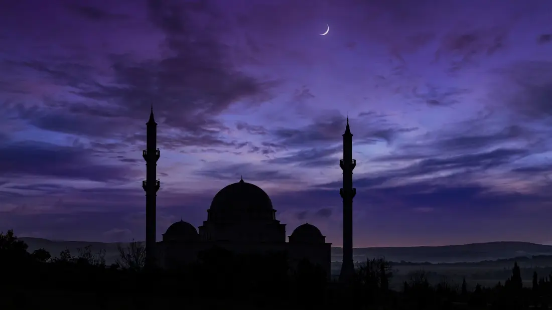 Mosque silhouette under a deep purple twilight sky with a crescent moon